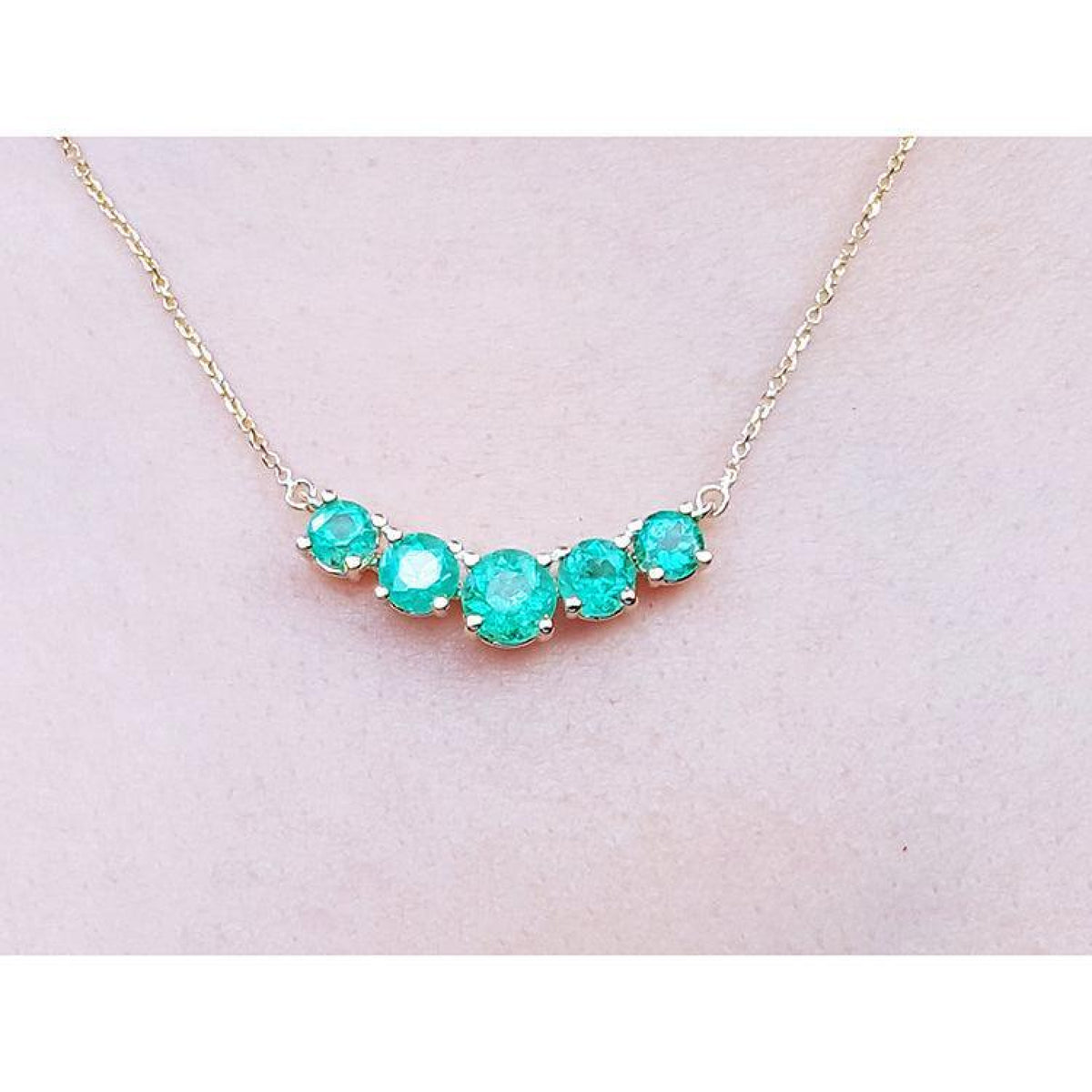 14K gold necklace with five round, medium green Colombian emeralds in elegant basket settings.