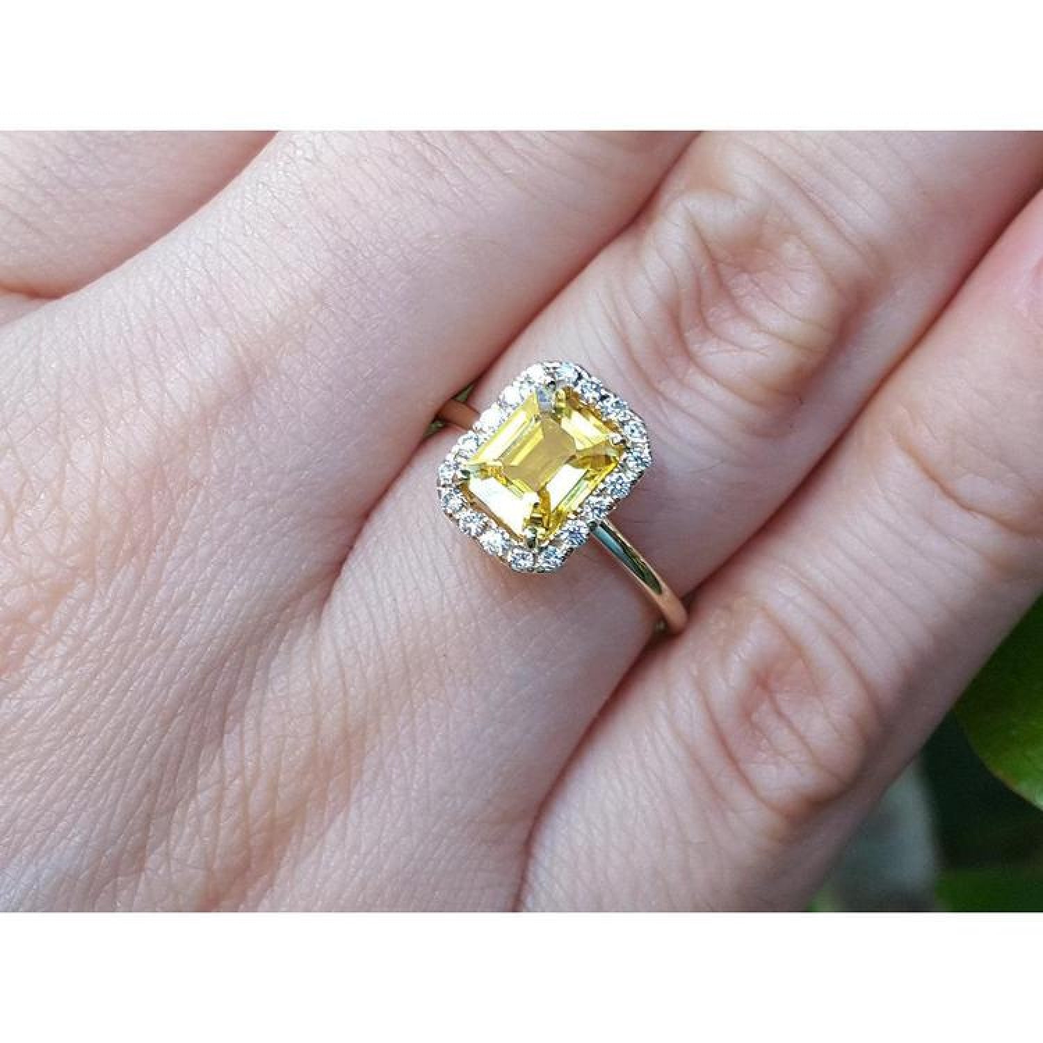 Emerald-cut natural yellow sapphire halo diamond ring in 14K yellow gold on a finger.