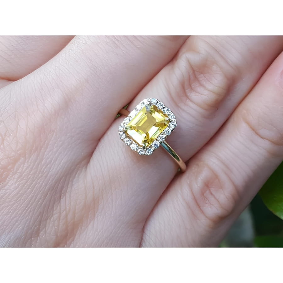 Emerald-cut natural yellow sapphire halo diamond ring in 14K yellow gold on a finger.