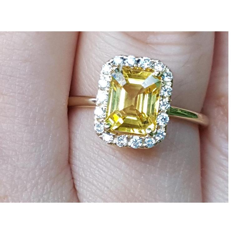 Gold ring with a yellow natural sapphire and halo diamond on a finger.