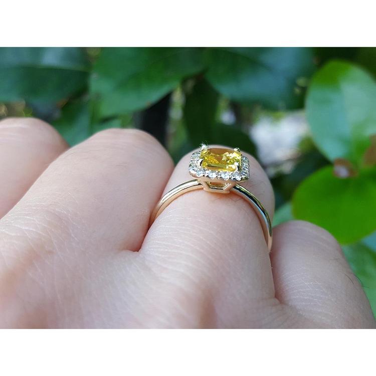 Gold ring with a yellow sapphire gemstone on a hand against a green leafy background
