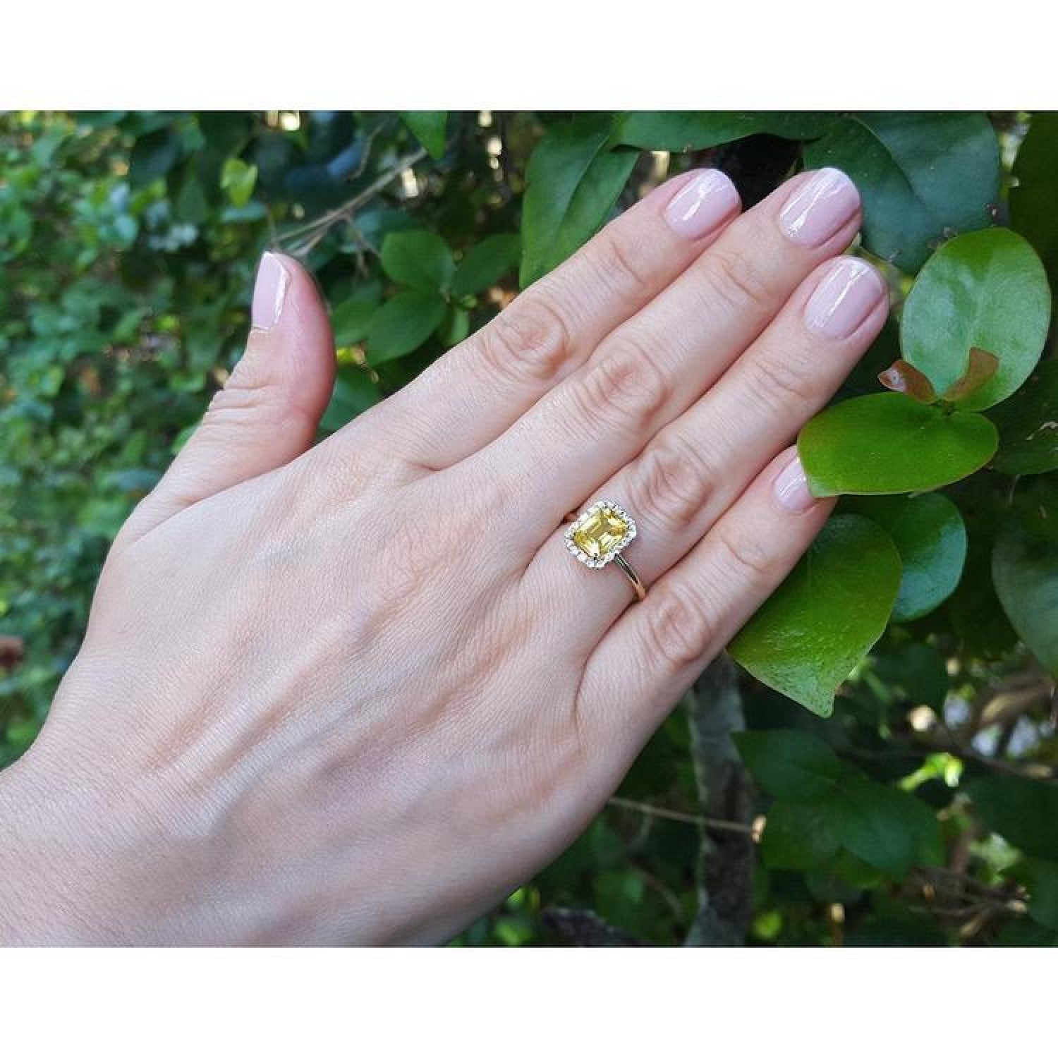 Emerald-cut natural yellow sapphire halo diamond ring in 14K yellow gold on a woman's hand.