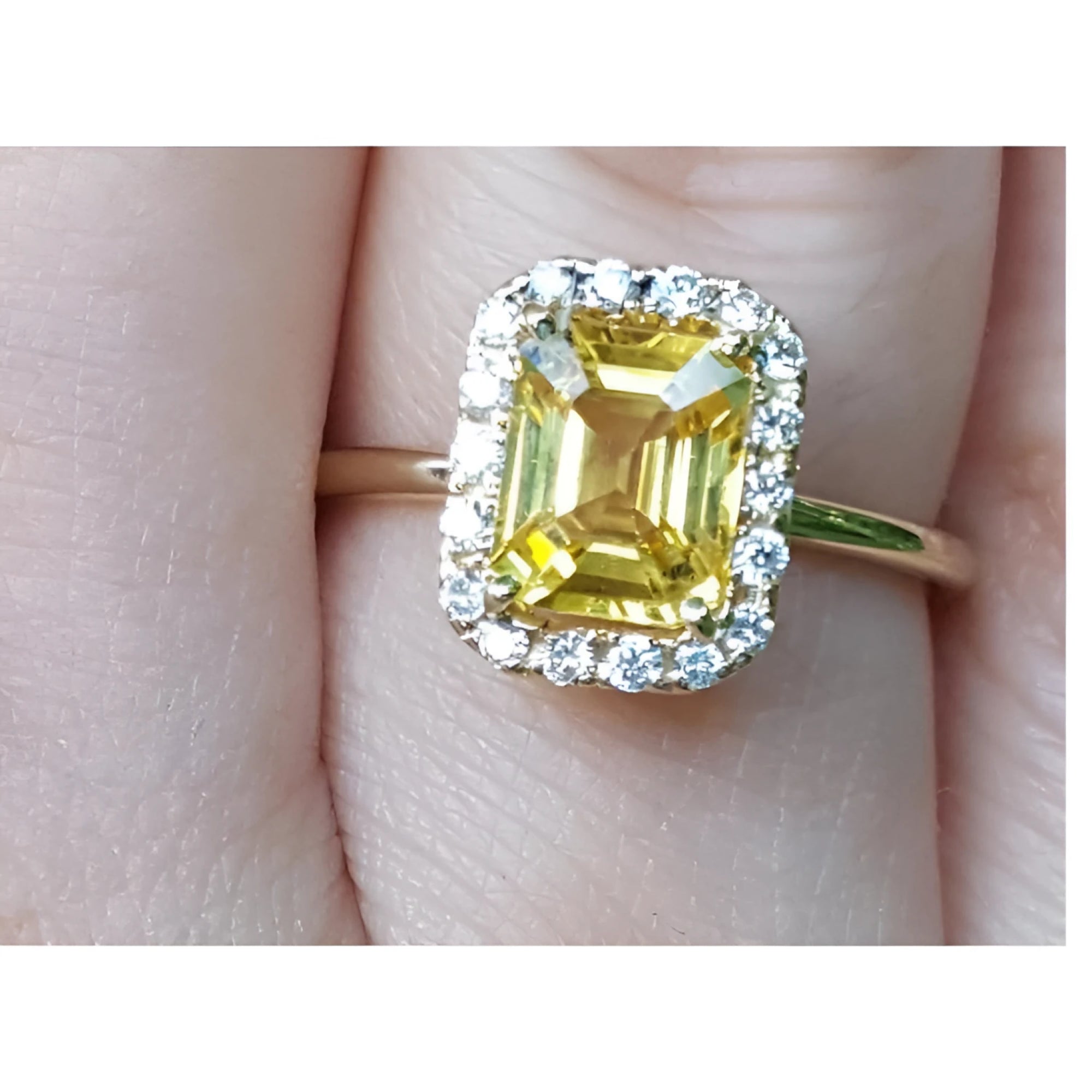 Gold ring with a yellow natural sapphire and halo diamond on a finger.