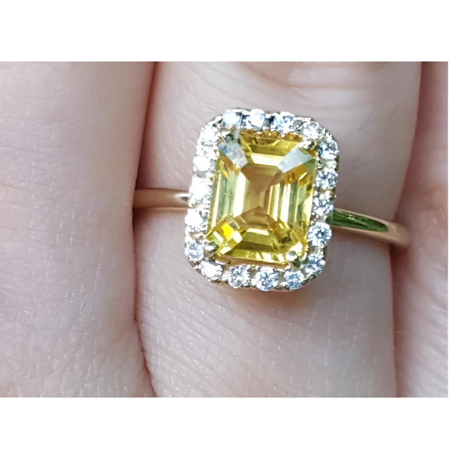 Gold ring with a yellow natural sapphire and halo diamond on a finger.