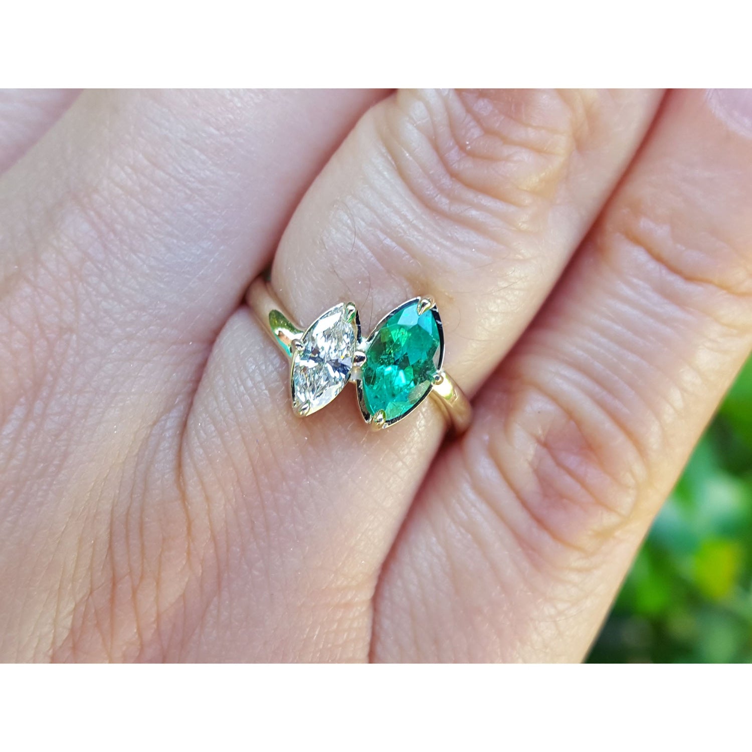 A toi et moi emerald and diamond ring marquise-cut you and me style made of 18k gold, shown worn on a person's finger.