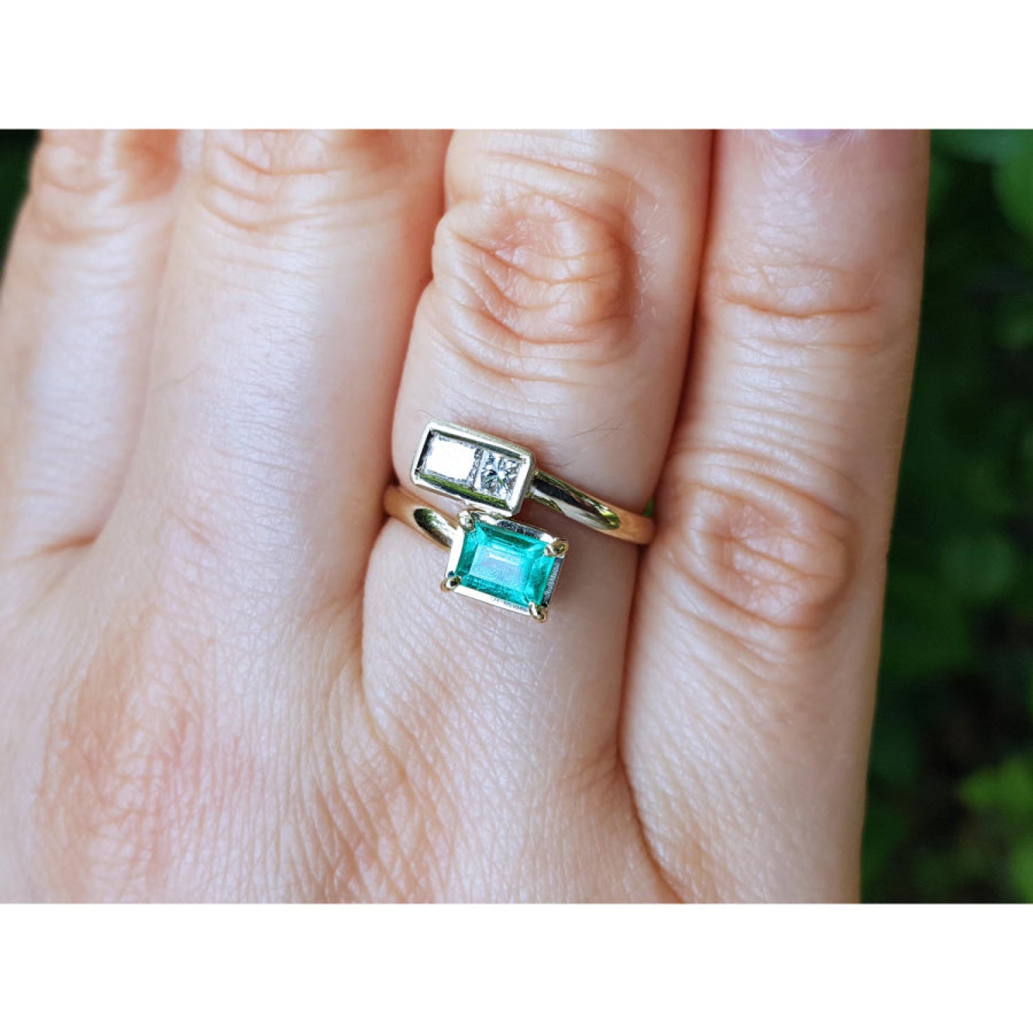 A gold you and me ring with a rectangular natural colombian emerald, shown worn on a person's finger.