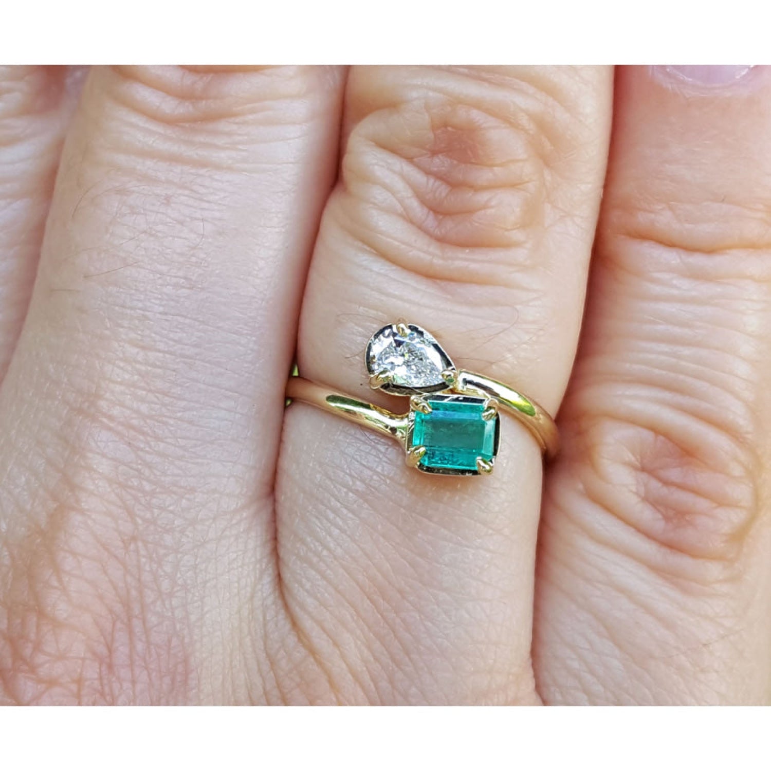 A 18k yellow gold you and me emerald and diamond ring, worn on a finger.