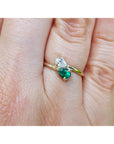 A gold ring with a diamond pear-cut gemstone and a natural emerald gemstone, shown worn on a person's finger.
