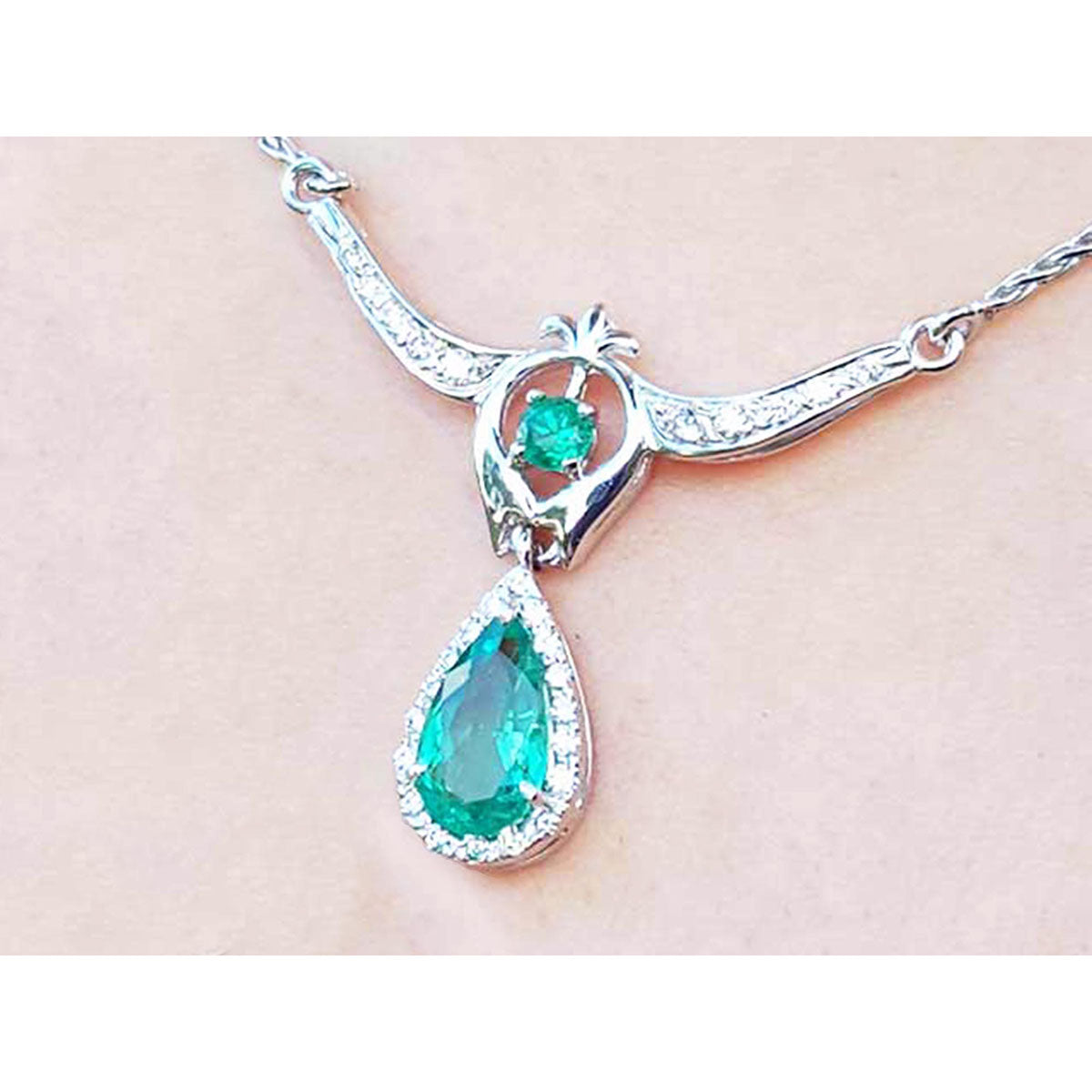 Zoom-in view of a white gold necklace with natural emerald teardrop pendant on a woman&#39;s collar