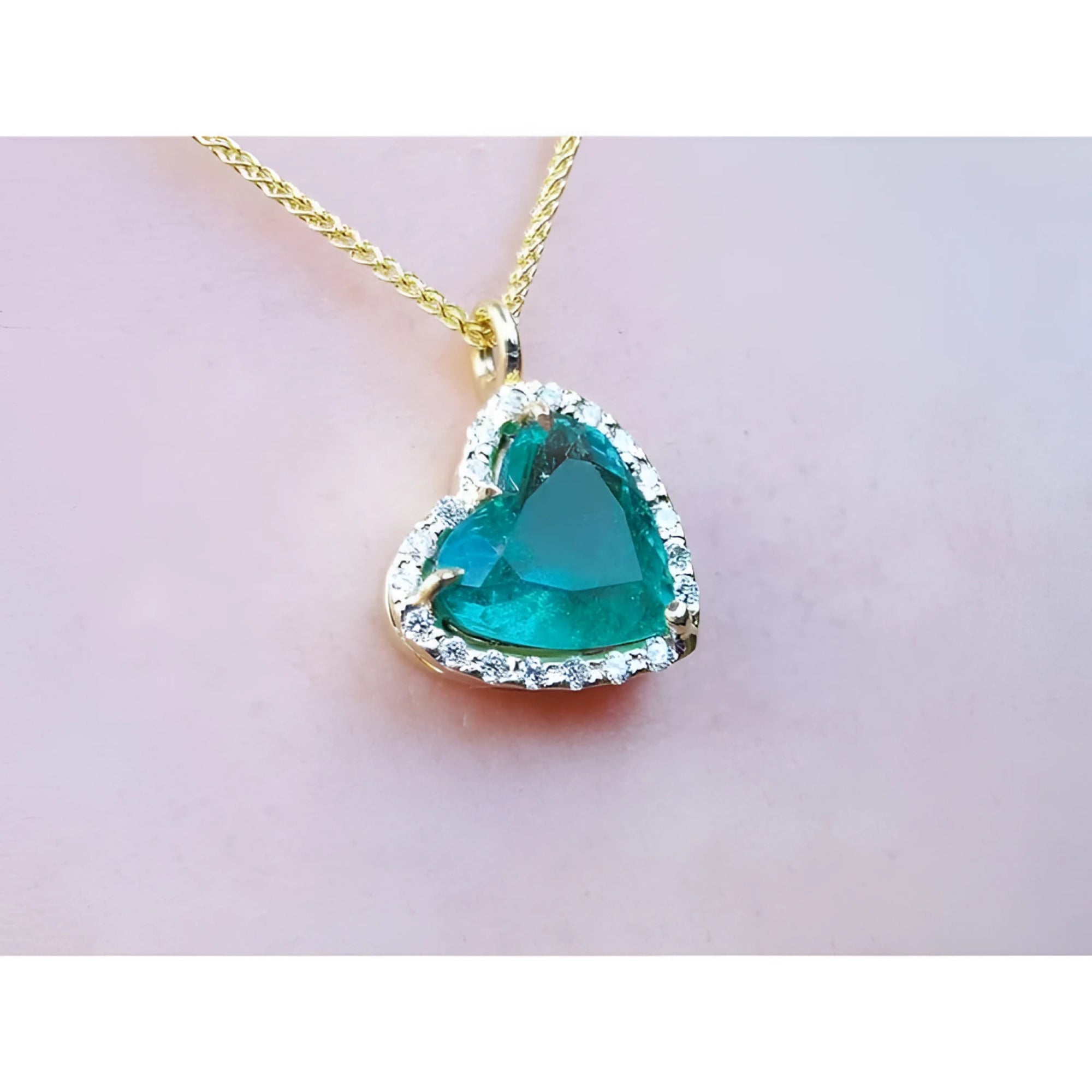 Tilted heart Colombian emerald necklace with halo diamonds on an 18K yellow gold chain.